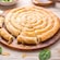A round spanakopita next to spinach and cheese on a wooden tabletop